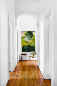 Green chair and wall art on a brown wood floor at the end of a long hallway with arches