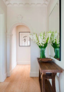 Brown wooden console table and floral vase beside an arched hallway